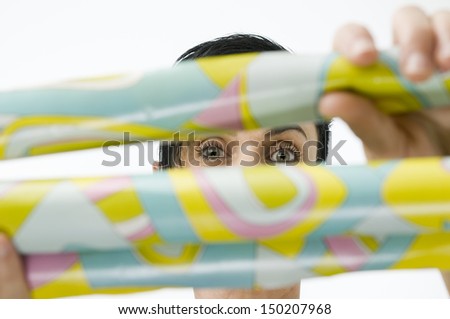 Head-and-shoulder view of a black-haired middle-aged woman with fuzzy pictured green yellow gift paper rolls held before him, that release only a slit on the illustrated sharp eyes behind