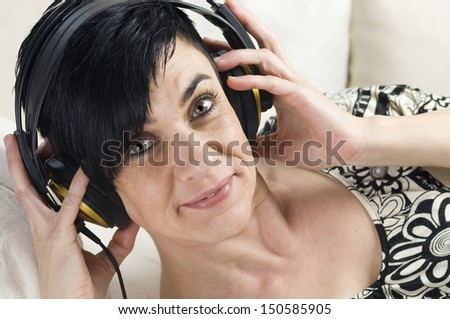Head and shoulder shot of a black-haired woman of middle age with hands on the headphones nicely into the camera looking