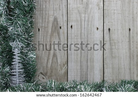 Green garland tinsel border with silver Christmas tree by wooden fence
