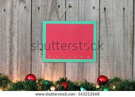 Red and green sign with decorated garland on wooden fence