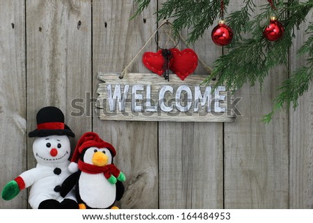 Wood welcome sign with holiday decorations - ornaments, red hearts, iron keys, penguin, snowman