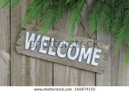 Wood welcome sign hanging on wood fence with evergreen border