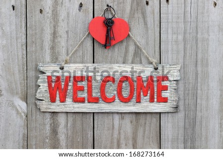 Red welcome sign hanging on wood door with red heart and iron keys