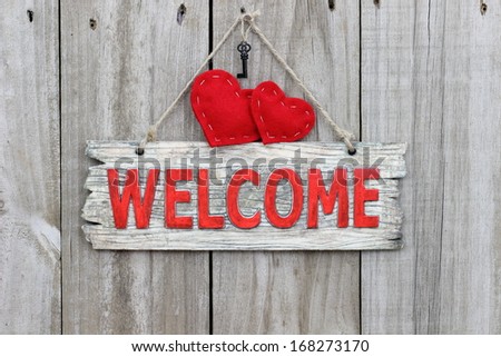 Red welcome sign hanging on wood door with red hearts and iron key