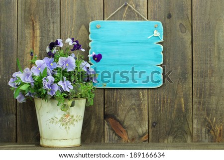 Antique blank blue sign with potted flowers (purple pansies) by wooden fence