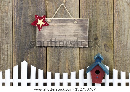 Blank wood sign over white picket fence with red and blue birdhouse