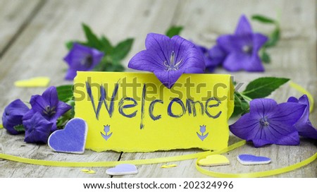 Welcome note card on wood table with purple flowers and hearts