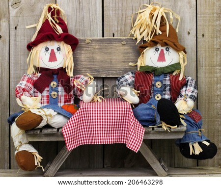 Boy and girl scarecrows sitting at picnic table by blank rustic wood sign