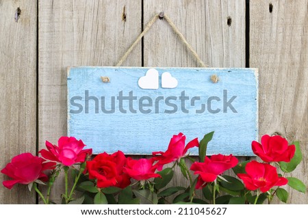 Flower border of red roses by antique blue blank sign with hearts hanging on fence