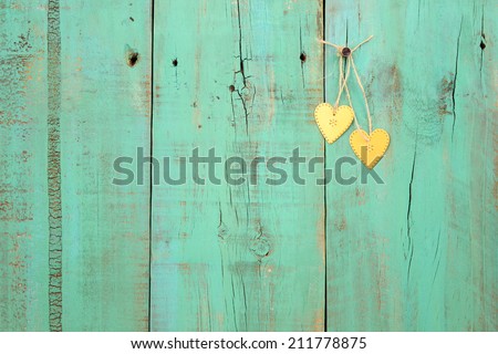 Two gold hearts hanging from rope on antique green weathered wood background