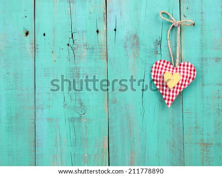 Red checkered and gold hearts hanging from rope on antique teal blue rustic wood background