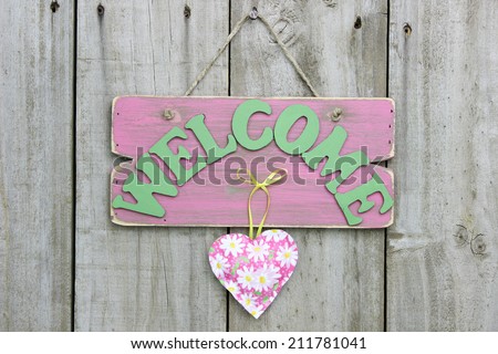 Distressed pink welcome sign with flower heart hanging on weathered wood fence
