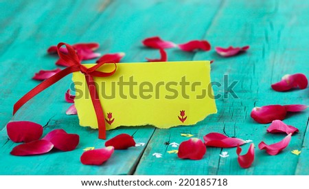 Blank yellow place card with red ribbon and flower petals on antique teal blue distressed wooden table