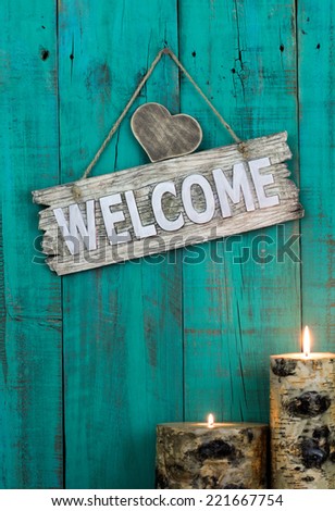 Wood welcome sign with heart and burning candles hanging on antique teal blue weathered wooden background