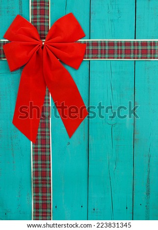Big red velvet bow with plaid ribbon on antique teal blue rustic wooden door