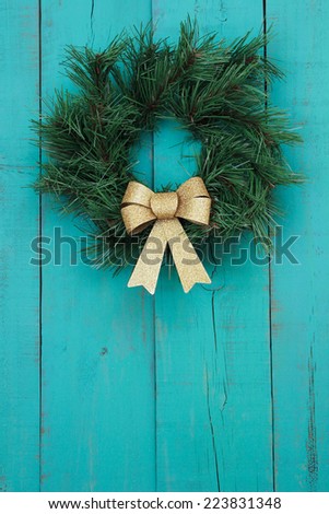Green wreath with gold bow on antique teal blue rustic wood door