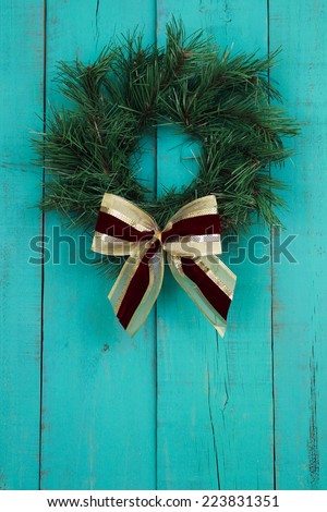 Green Christmas wreath with red and gold bow on antique teal blue old rustic wooden door