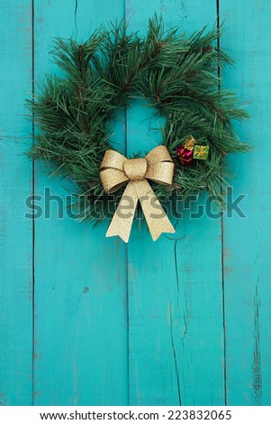 Green wreath with gold bow and presents hanging on antique teal blue rustic wooden door