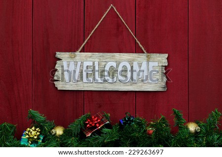 Rustic welcome sign with Christmas garland border and gifts hanging on antique red wooden background