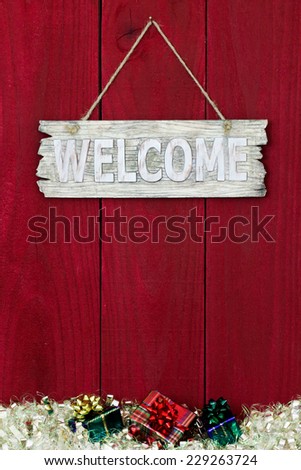 Welcome sign with Christmas garland border and presents hanging on antique red wooden background