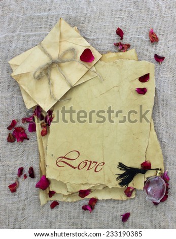 Worn antique parchment paper love letters and envelopes tied in rope with red rose petals and perfume bottle on rustic background
