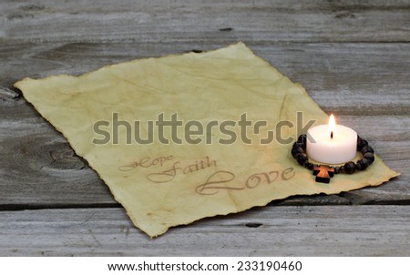 Burning candle and wooden cross on antique parchment paper with Hope, Faith, Love with rustic wooden background