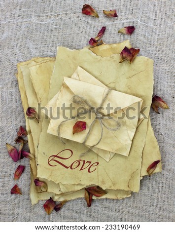 Worn antique parchment paper love letters and envelopes tied in rope by dried rose petals on rustic background