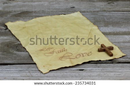 Antique parchment paper letter with HOPE, FAITH, LOVE text and wood cross on weathered wooden background