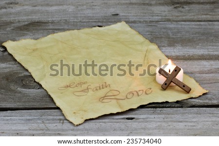 Antique parchment paper letter with HOPE, FAITH LOVE text, wood cross and burning candle on rugged wooden background