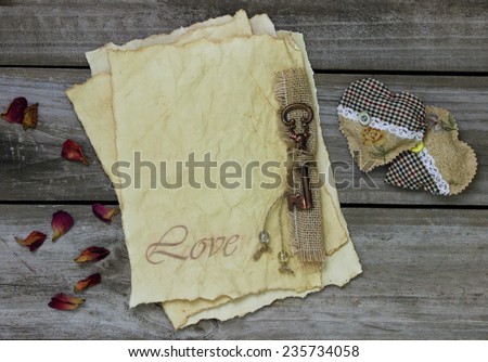 Antique parchment paper love letters with bronze skeleton key, rose petals and fabric hearts on rustic wooden background