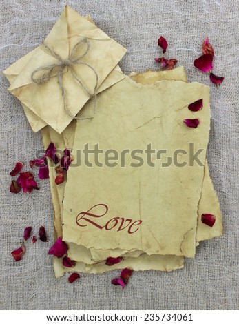 Antique parchment paper love letters and envelopes tied in rope with rose petals on textured background