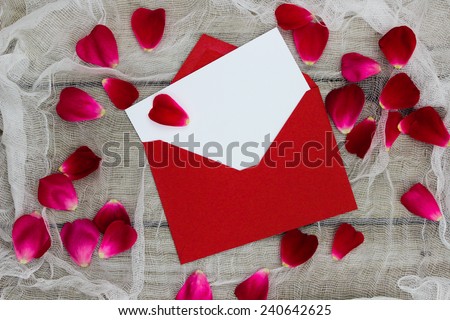Blank white love letter or note card and red envelope with red flower petals on shabby white netting and wood background