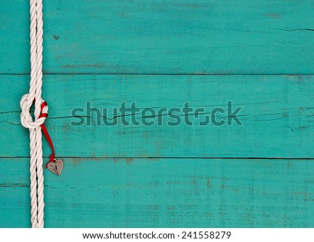 Silver heart lock hanging by red ribbon on white rope with knot border against blank antique teal blue old weathered background