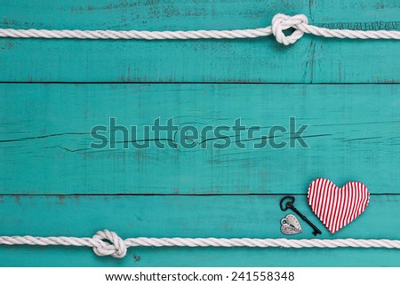 Silver lock, red candy cane striped heart and black iron key by white rope with knot border against blank antique teal blue weathered background
