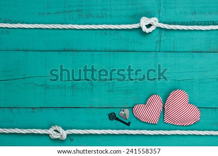 Red and white candy cane striped hearts, silver lock and black iron key by white rope with knot border against blank antique teal blue shabby wooden background