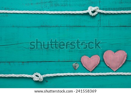 Red and white candy cane striped hearts and silver heart lock by rope with knot border on blank antique teal blue shabby wooden background