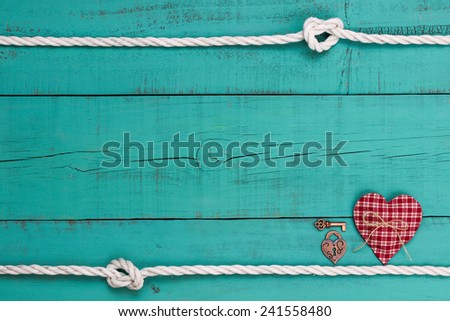 Red checkered heart, bronze key and lock by white rope with knot border against blank antique teal blue shabby wood background