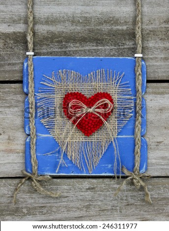 Antique blue wood sign with red fabric and burlap heats hanging by braided rope on distressed wooded door