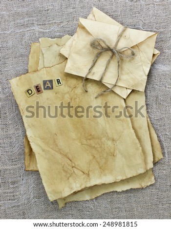 Collection of antique parchment paper letters with the word Dear and envelopes tied in rope on shabby netting background