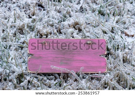 Blank pink wooden sign with ice covered grass after ice storm background