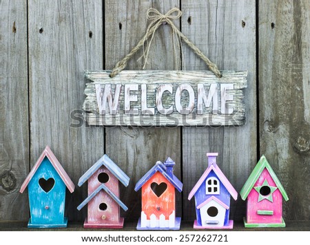 Welcome sign hanging over row of colorful pastel birdhouses with rustic wooden background
