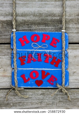 Antique blue sign with red HOPE, FAITH, LOVE and heart hanging by braided rope on rustic wood background