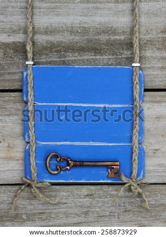Blank antique blue sign with bronze skeleton key hanging by braided rope on rustic wood background