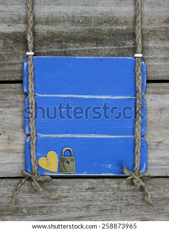 Blank antique blue sign with gold heart and lock hanging by braided rope on rustic wood background