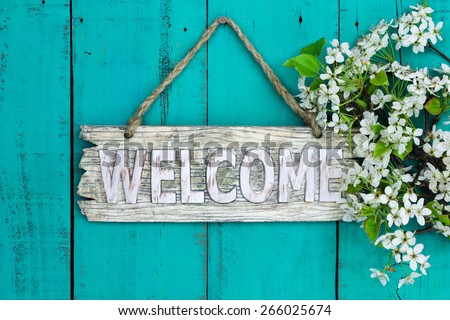 Wooden welcome sign with spring tree blossoms border hanging on antique teal blue wood background