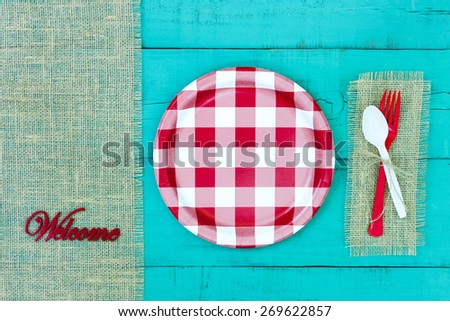Welcome sign with red and white checkered plate and burlap border on antique teal blue wood background; above view looking down