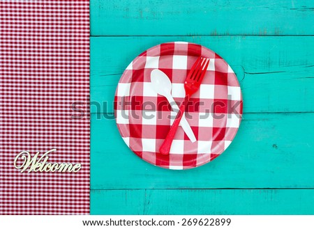 Welcome sign with red and white checkered plate and gingham border on antique teal blue wood background; above view looking down
