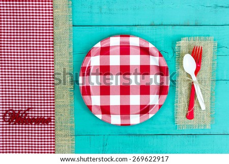 Welcome sign with red and white checkered plate and gingham and burlap border on antique teal blue wood background; above view looking down