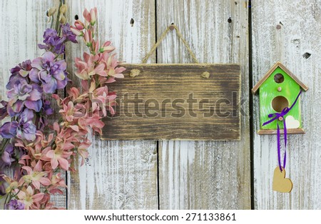 Blank wood sign hanging on white fence by spring flowers and green birdhouse with hearts