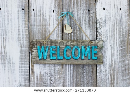 Teal blue welcome sign with wooden hearts hanging on white painted weathered wood fence